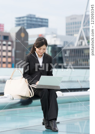 A smiling businesswoman looking at a laptop outdoors at the Water Spaceship, OASIS21, Sakae, Nagoya A smiling businesswoman looking at a laptop outdoors at the Water Spaceship, OASIS21, Sakae, Nagoya 123093345