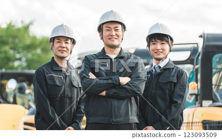 一名在建築業工作的男性商人，穿著工作服，站在重型機械前 123093509