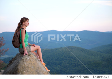Sportive female hiker sitting alone taking a break on hillside trail. Lonely woman enjoying view of summer nature from rocky cliff on wilderness path. Active lifestyle concept 123093875