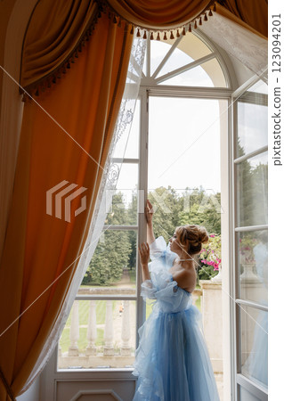 Elegant woman in a light blue ball gown in a luxurious classic interior plays a white piano 123094201