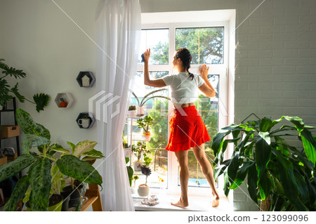 Woman manually washes the window of house with rag cleaner and mop inside the interior with home plants on windowsill. Restoring order and cleanliness in the spring, cleaning servise 123099096