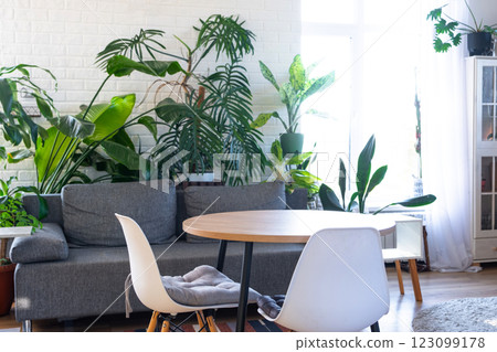 Modern loft-style village interior of house with large potted plants, gray sofa, empty round table, a striped rug, and large windows. 123099178