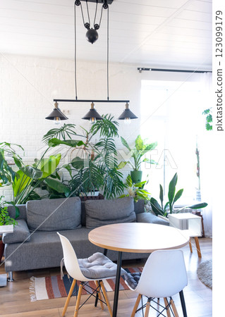 Modern loft-style village interior of house with large potted plants, gray sofa, empty round table, a striped rug, and large windows. Modern loft-style village interior of house with large potted plants, gray sofa, empty round table, a striped rug, and large windows. 123099179
