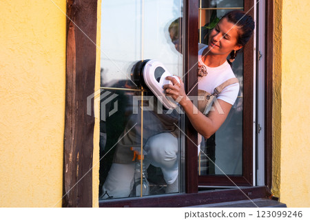 A woman launches window cleaner robot of house outside with a yellow facade. Household robotics, household assistant, cleaning servise A woman launches window cleaner robot of house outside with a yellow facade. Household robotics, household assistant, cleaning servise 123099246