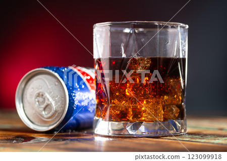 Can of cola and glass of whiskey with ice cubes on red and blue background Can of cola and glass of whiskey with ice cubes on red and blue background 123099918