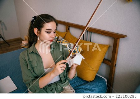 A young woman applies rosin to a violin bow, preparing for a practice session. A dedicated violinist carefully maintains her bow to ensure better sound quality and smooth playing. 123100283