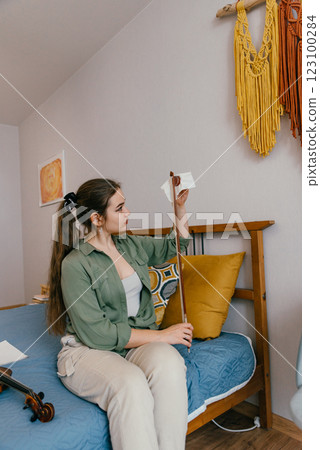 A young woman applies rosin to a violin bow, preparing for a practice session. A dedicated violinist carefully maintains her bow to ensure better sound quality and smooth playing. 123100284
