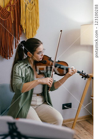 Violin student playing notes at home, preparing for a future performance. A young musician sharpens her violin skills during an intensive rehearsal Violin student playing notes at home, preparing for a future performance. A young musician sharpens her violin skills during an intensive rehearsal 123100288