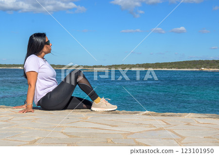 Woman sitting by the ocean, looking relaxed and peaceful, dressed casually on a sunny day, beautiful latina woman by the sea 123101950