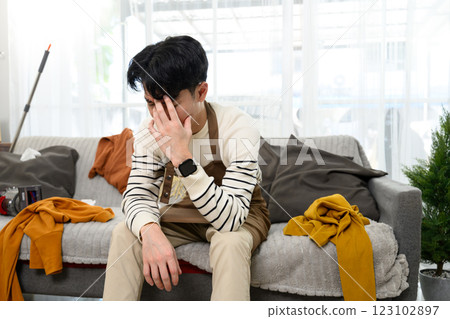 Tired and upset man sitting on couch in messy living room Tired and upset man sitting on couch in messy living room 123102897