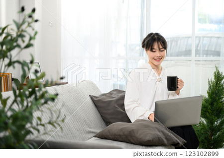 Cheerful asian woman sipping coffee and working on her laptop Cheerful asian woman sipping coffee and working on her laptop 123102899