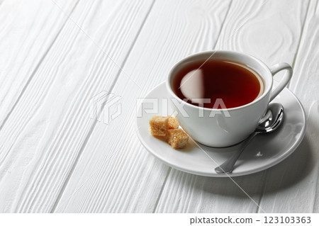 black tea in cup on saucer with spoon and sugar cubes on white wooden table black tea in cup on saucer with spoon and sugar cubes on white wooden table 123103363
