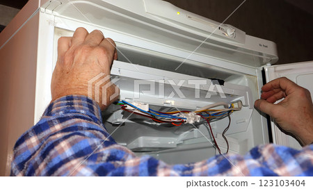 Repairing a refrigerator with complex wiring inside a kitchen setting during the daytime Repairing a refrigerator with complex wiring inside a kitchen setting during the daytime 123103404