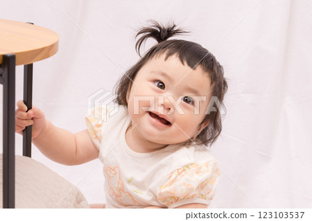 [Baby with twin tails standing up holding onto a table] 123103537