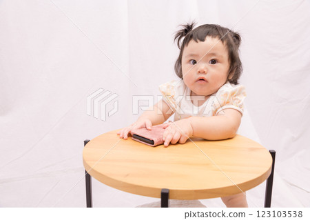 [Pigtailed baby standing on a table with smartphone] 123103538