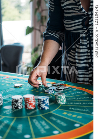 Hand placing a poker chip on a wine-themed casino game mat, blending gambling and wine culture for a unique entertainment experience Hand placing a poker chip on a wine-themed casino game mat, blending gambling and wine culture for a unique entertainment experience 123104245