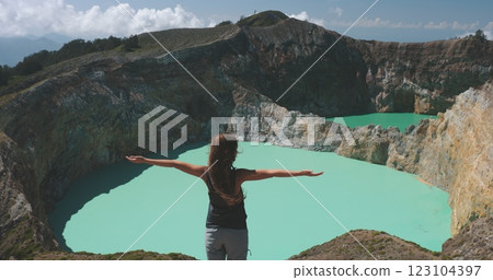Woman stands at a turquoise crater lake, embracing the stunning view of a volcanic landscape, inviting viewers to explore and discover the serene setting Woman stands at a turquoise crater lake, embracing the stunning view of a volcanic landscape, inviting viewers to explore and discover the serene setting 123104397
