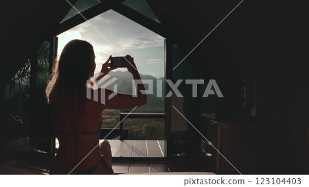 Capturing the sunset view of a mountain range from a bungalow in thailand, a woman enjoys her vacation, sharing moments of happiness and inspiration on social media 123104403