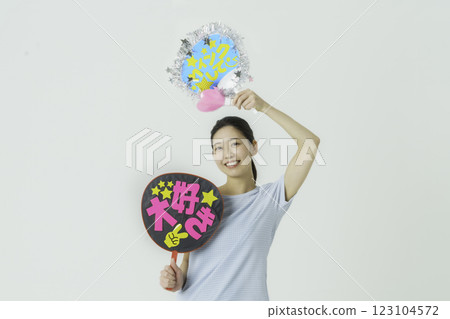 Oshikatsu: A young woman cheering on her idol with a fan on a white background 123104572