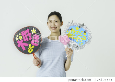 Oshikatsu: A young woman cheering on her idol with a fan on a white background 123104573