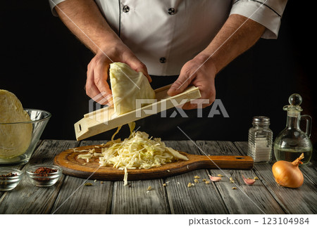 In a cozy kitchen, a chef expertly shreds fresh cabbage using a mandoline. Surrounding ingredients include onions, garlic, and spices, hinting at a flavorful recipe in progress In a cozy kitchen, a chef expertly shreds fresh cabbage using a mandoline. Surrounding ingredients include onions, garlic, and spices, hinting at a flavorful recipe in progress 123104984