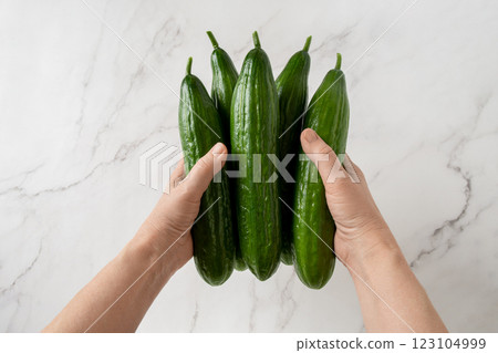 Woman hands hold green cucumbers over marble countertop. 123104999