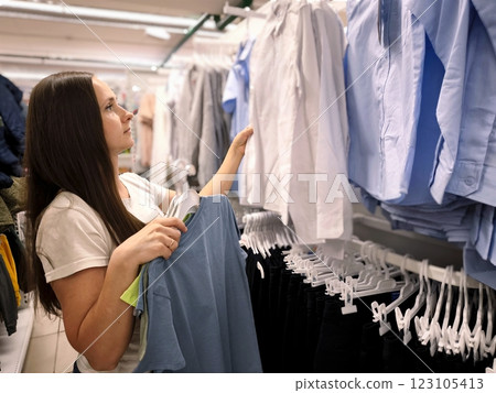 A young woman with long dark hair is choosing clothes for a child in a store A young woman with long dark hair is choosing clothes for a child in a store 123105413