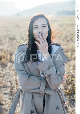 Beautiful fashionable brunette woman in gray coat smoking a cigarette Beautiful fashionable brunette woman in gray coat smoking a cigarette 123105942