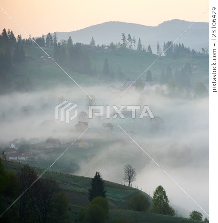 Village enveloped in morning mist. Houses and trees emerge softly from fog, creating dreamy and tranquil atmosphere. Rolling green hills and dense forests add depth and contrast to scene. Village enveloped in morning mist. Houses and trees emerge softly from fog, creating dreamy and tranquil atmosphere. Rolling green hills and dense forests add depth and contrast to scene. 123106429