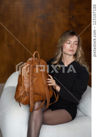 A girl in a warm sweater, a black short skirt, nylon tights, and black shoes is posing with a brown backpack. A girl in a warm sweater, a black short skirt, nylon tights, and black shoes is posing with a brown backpack. 123107188