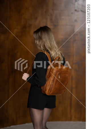 A girl in a warm sweater, a black short skirt and nylon tights is posing with a brown backpack. 123107203