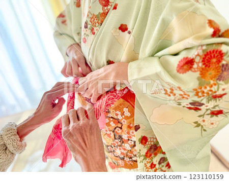 Two women putting on obiage during a kimono dressing session 123110159
