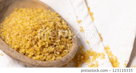 Raw dry uncooked yellow bulgur grain in a wooden bowl on white table cloesup. Ancient food Raw dry uncooked yellow bulgur grain in a wooden bowl on white table cloesup. Ancient food 123110335