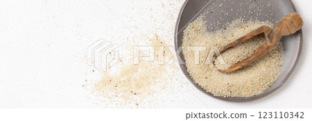 Raw uncooked fonio seeds on grey plate with a wooden spoon on white table topview. African cereal Raw uncooked fonio seeds on grey plate with a wooden spoon on white table topview. African cereal 123110342