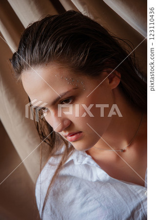 Thoughtful young woman with glitter makeup in natural light setting. Caucasian woman with glitter on face. Beige background 123110436