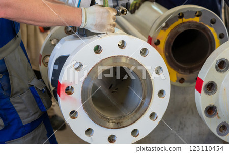 Worker dismantling an ultrasonic flowmeter from a flanged pipeline in an industrial setting. Worker dismantling an ultrasonic flowmeter from a flanged pipeline in an industrial setting. 123110454