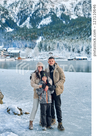 Winter Family Adventure: Parents and Child Exploring Snowy Mountain Landscape with Frozen Lake and Alpine Village Winter Family Adventure: Parents and Child Exploring Snowy Mountain Landscape with Frozen Lake and Alpine Village 123110646