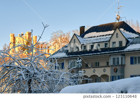 Charming Winter Wonderland: Snow-Covered European Village House with Blue Roof and Medieval Castle Backdrop in Golden Sunlight Charming Winter Wonderland: Snow-Covered European Village House with Blue Roof and Medieval Castle Backdrop in Golden Sunlight 123110648