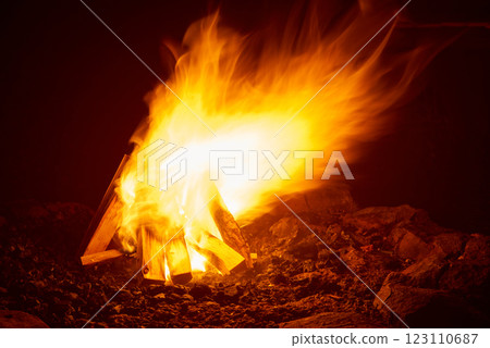 Vibrant campfire flames illuminate dark wilderness night with bright orange glow and dancing fire tongues. Traditional outdoor bonfire with burning wood logs creates warm atmospheric light perfect for 123110687