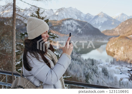 Winter Wanderlust: Young Woman Using Smartphone in Snowy Mountain Landscape with Golden Sunlight and Picturesque Village Winter Wanderlust: Young Woman Using Smartphone in Snowy Mountain Landscape with Golden Sunlight and Picturesque Village 123110691