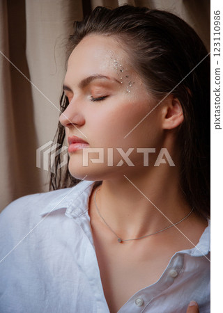 Serene portrait of a woman with glitter makeup in natural light. Caucasian woman with glitter on face. Beige background Serene portrait of a woman with glitter makeup in natural light. Caucasian woman with glitter on face. Beige background 123110986