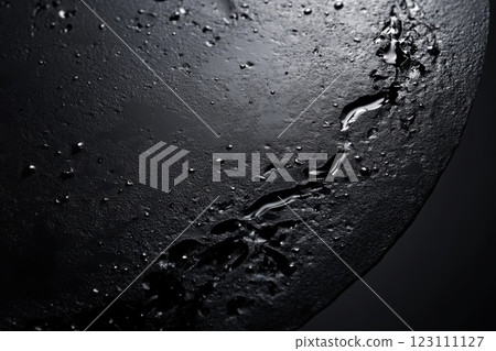 Dark surface with water droplets and a single flowing stream highlighted in dramatic lighting creates an artistic mood in a studio environment Dark surface with water droplets and a single flowing stream highlighted in dramatic lighting creates an artistic mood in a studio environment 123111127