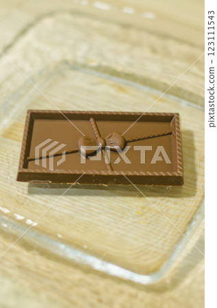 Chocolate bar with a decorative bow on a glass plate over a wooden surface. High quality photo 123111543