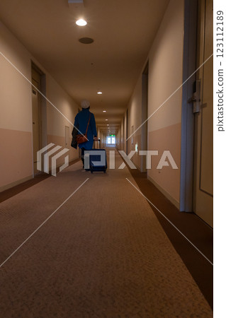 一位女士拉著行李箱走在飯店走廊的背影 123112189