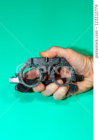 Female hands holding optical device for vision examination on a green surface. Female hands holding optical device for vision examination on a green surface. 123112774