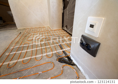 Heating red electrical cable wire system installed on cement floor in small new unfinished room with plastered walls. Renovation and construction, modern technology, comfortable warm home concept. 123114131