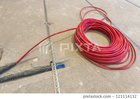 Heating red electrical cable wire roll on cement floor copy space background. Renovation and construction, comfortable warm home concept. 123114132