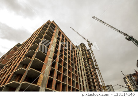 Ground view of a new modern residential house building under construction. Real estate development concept. Multi story home from bricks and concrete. Construction site tower crane at work. 123114140