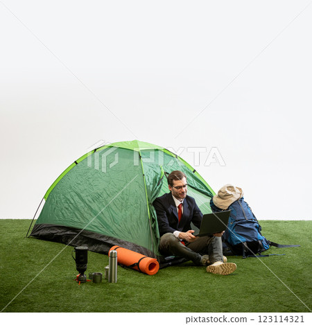 Businessman sitting on camping mat near tent holding laptop and coffee mug against white studio background. 123114321