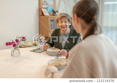 Senior woman enjoying meal with younger female family member at home. Concept of family bonding, aging, and healthy eating. Grandmother spending quality time with granddaugther at home. Senior woman enjoying meal with younger female family member at home. Concept of family bonding, aging, and healthy eating. Grandmother spending quality time with granddaugther at home. 123114376